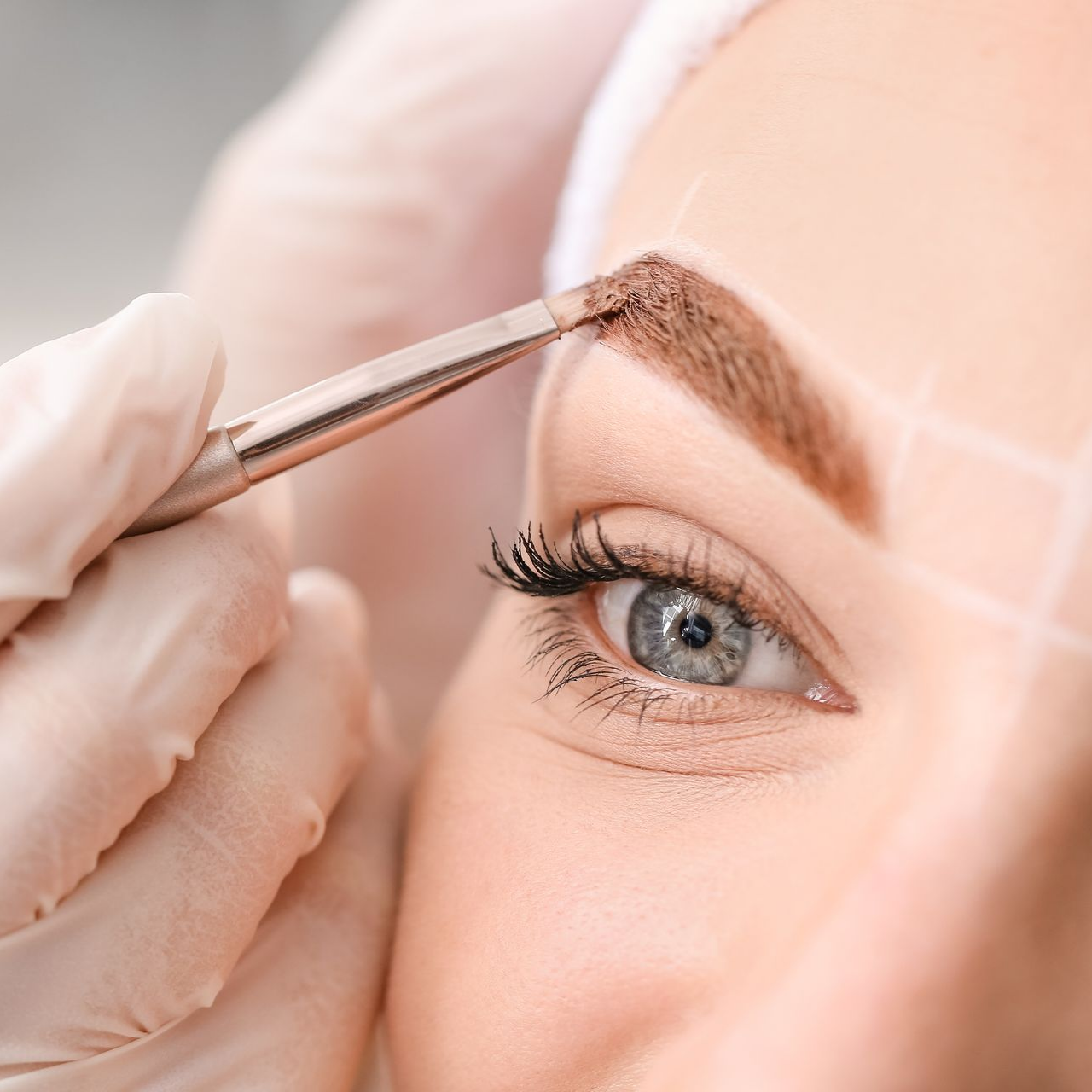 Esthéticienne en train de poser de la teinture sur les sourcils d'une cliente avec un pinceau