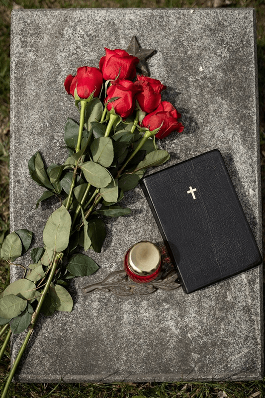 Rote Rosen, eine schwarze Bibel und eine Kerze liegen auf einem grauen Grabstein.