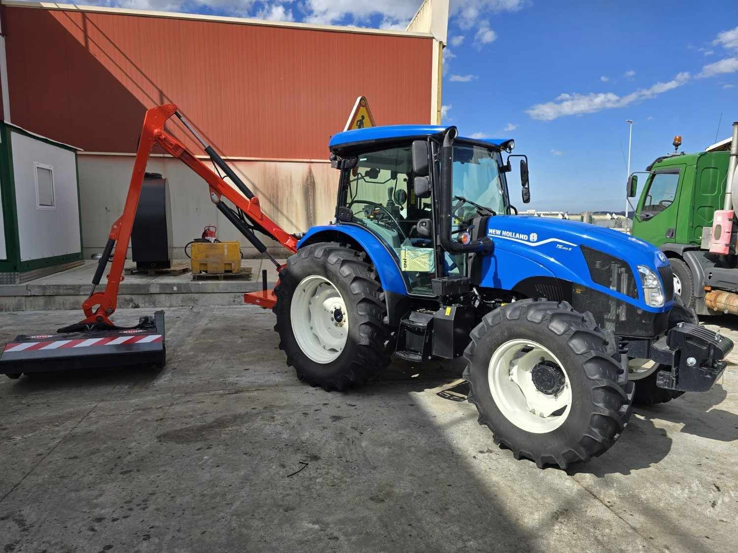 Una excavadora amarilla está estacionada junto a un tractor verde frente a un edificio.