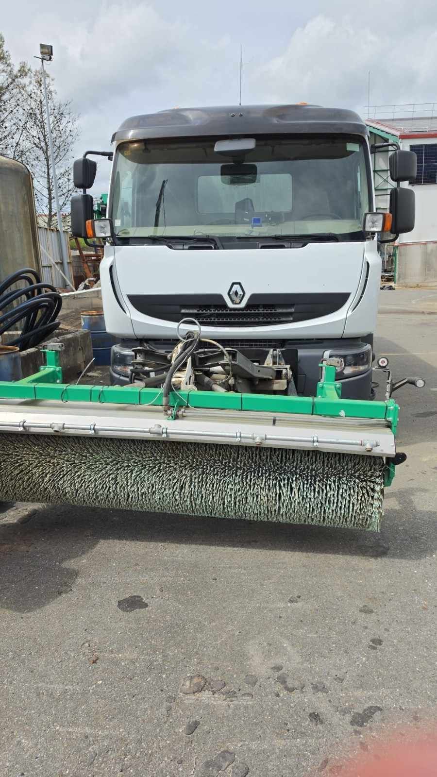 Camión utilitario blanco con un cepillo barredor de calles montado en la parte delantera en una carretera.