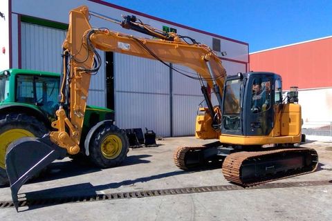 Una excavadora amarilla está estacionada junto a un tractor verde frente a un edificio.