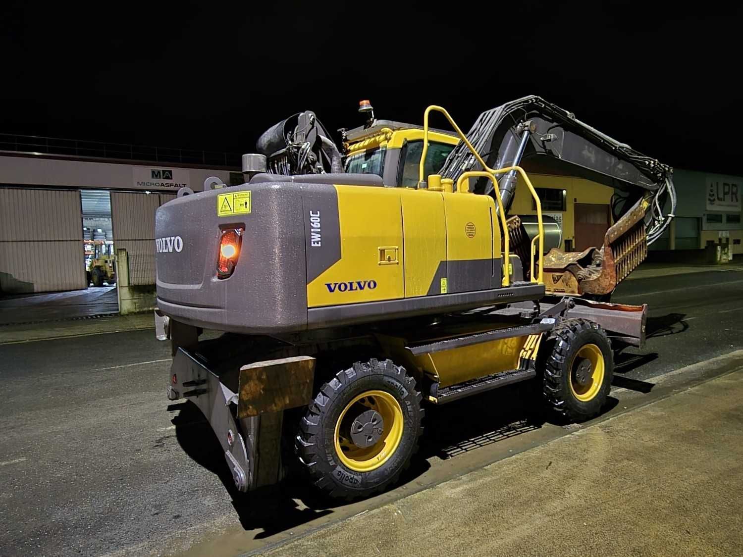 Excavadora amarilla sobre un remolque de plataforma plana de noche en un estacionamiento.