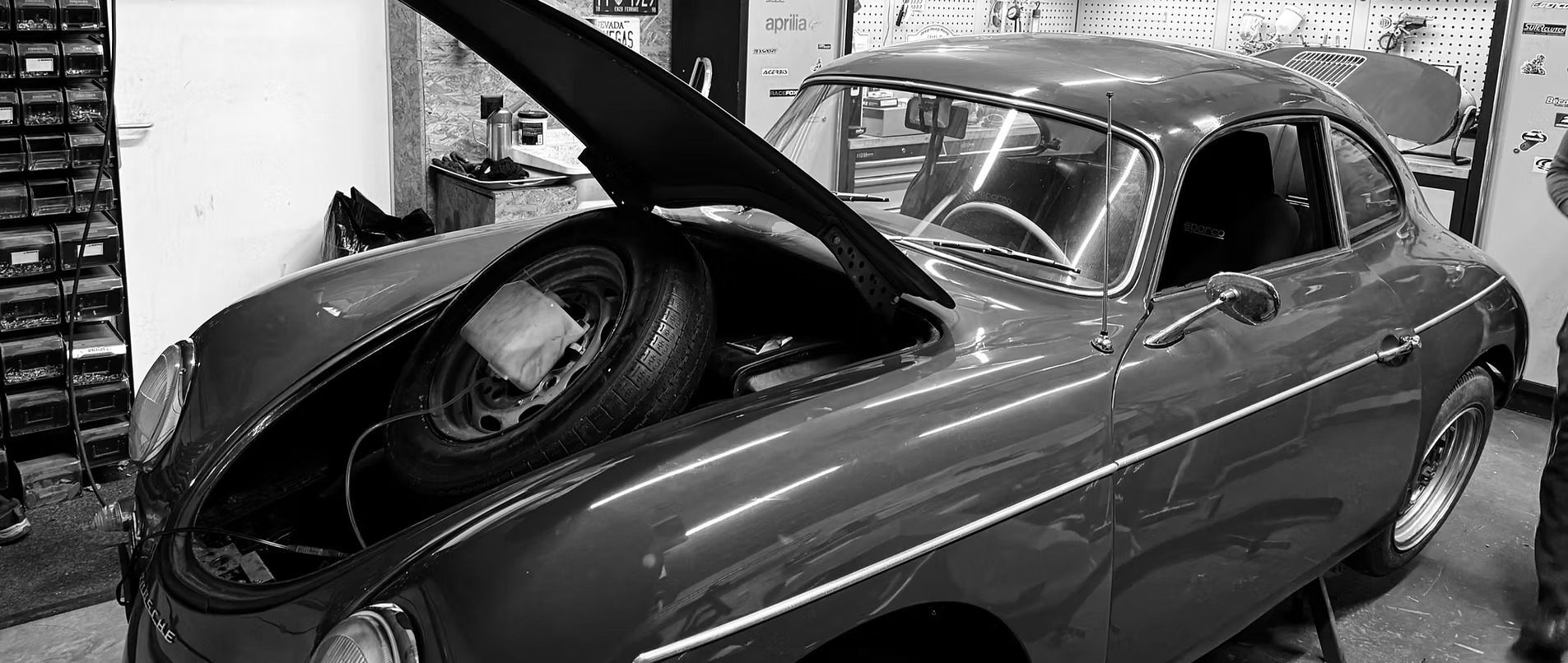 Une voiture de collection, capot ouvert, laissant apparaître une roue de secours. Photo en noir et blanc.