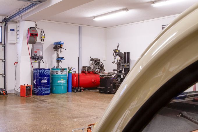 Un mécanicien en combinaison grise utilise une clé à chocs sur un pneu de voiture dans un garage.