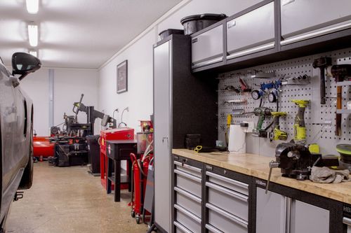 Voiture blanche, phares allumés, dans un garage sombre à porte ouverte, éclairé par des plafonniers.