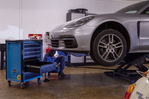 Un mécanicien en combinaison grise utilise une clé à chocs sur un pneu de voiture dans un garage.
