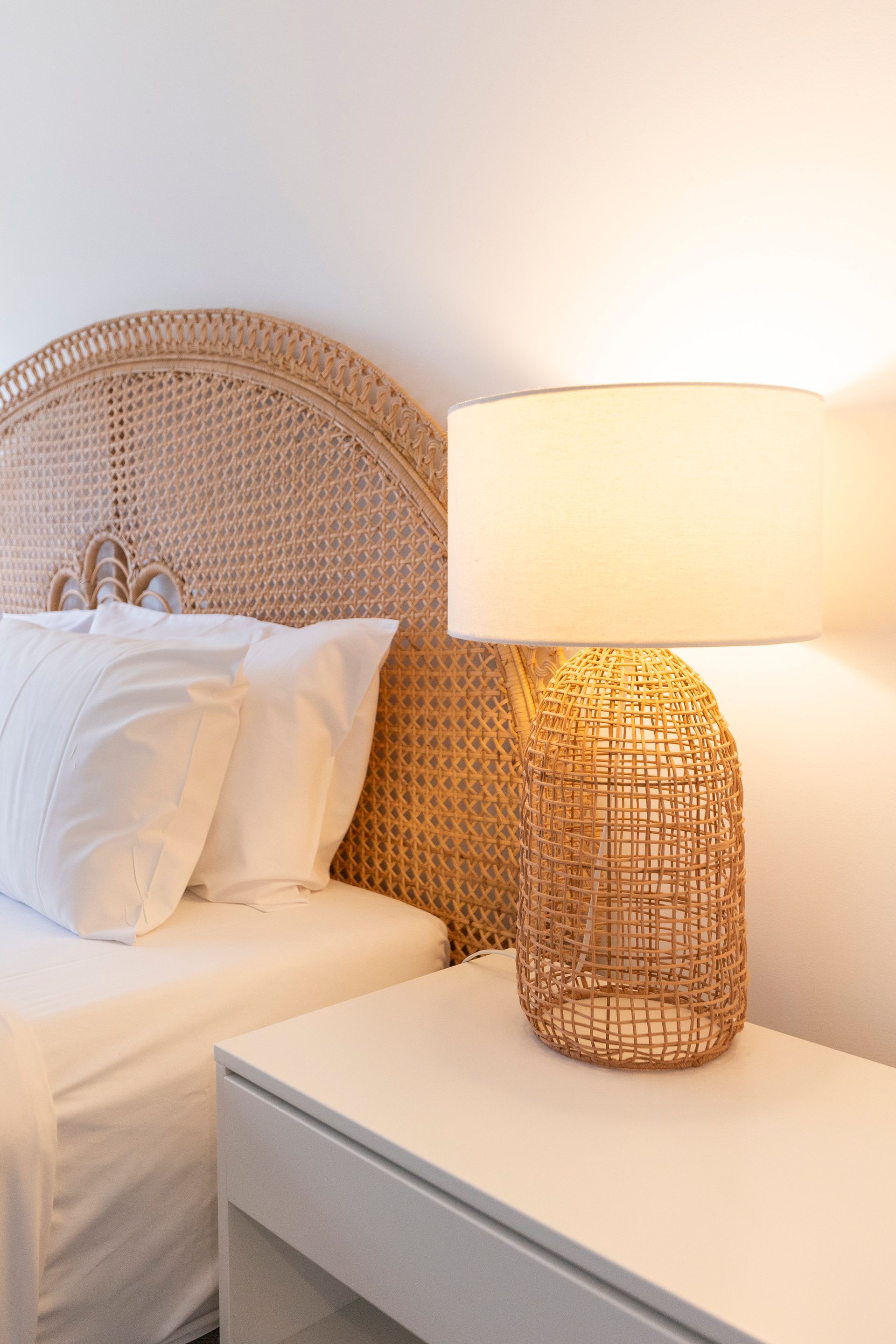 A bedroom with a bed , nightstand , lamp and wicker headboard.