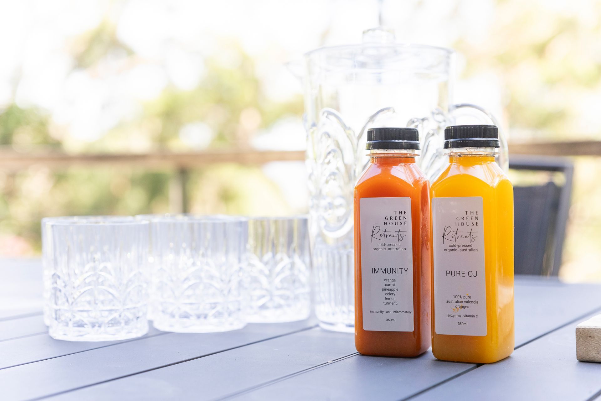 Two bottles of juice are sitting on a table next to a pitcher and glasses.