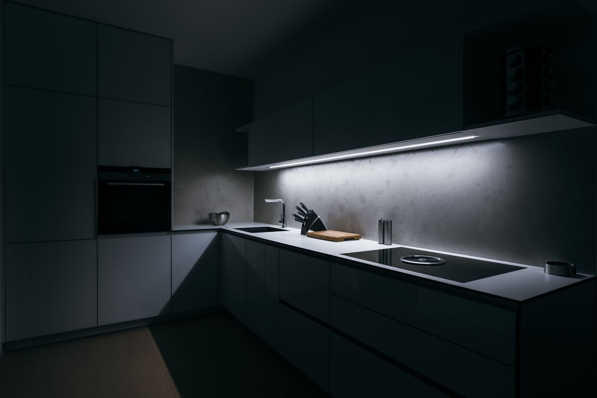 Cuisine moderne sombre avec un comptoir, un évier et un éclairage sous les armoires aux lignes épurées.