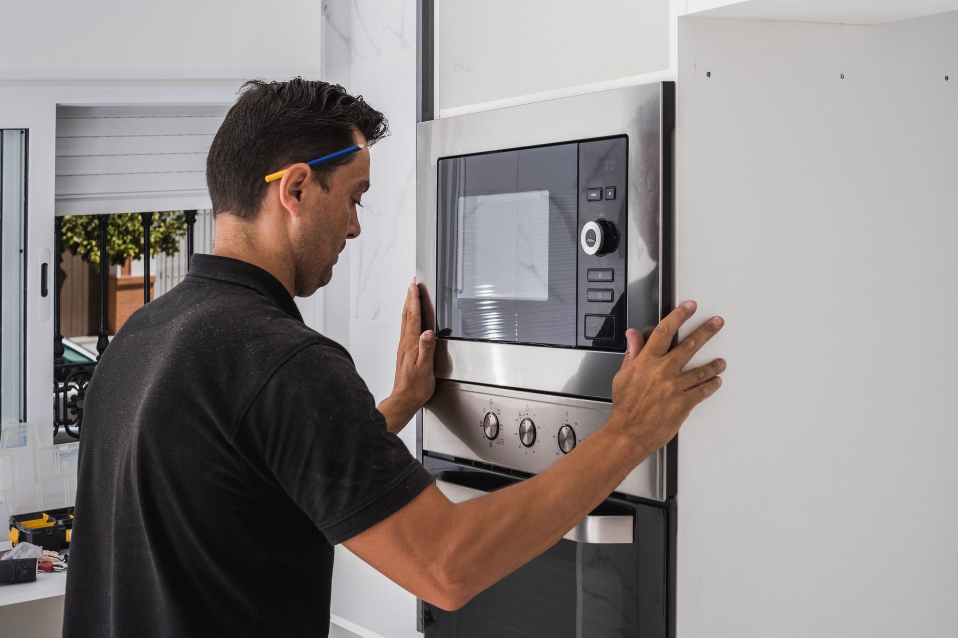 Deux ouvriers installent des meubles de cuisine dans une cuisine lumineuse, l'un sur une échelle et l'autre accroupi avec des outils.