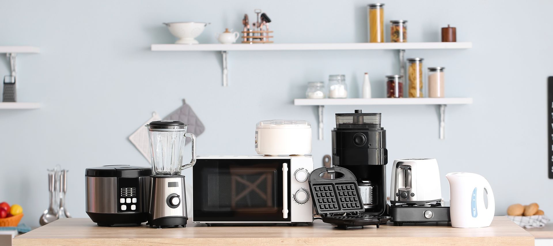 Comptoir de cuisine avec cafetière, mini-four, bouilloire et tasses sous des étagères blanches