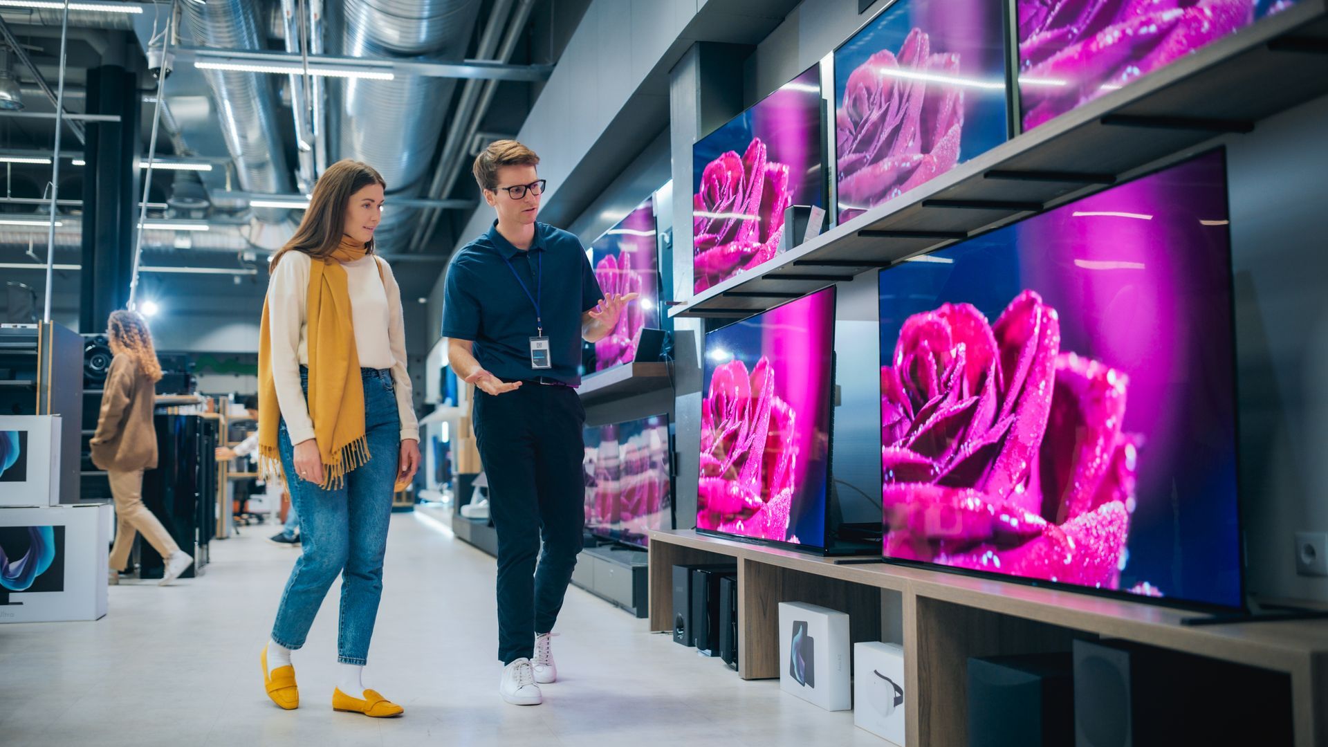 Deux personnes parcourent les rayons d'un magasin d'électronique moderne, exposant des produits d'un magenta éclatant.