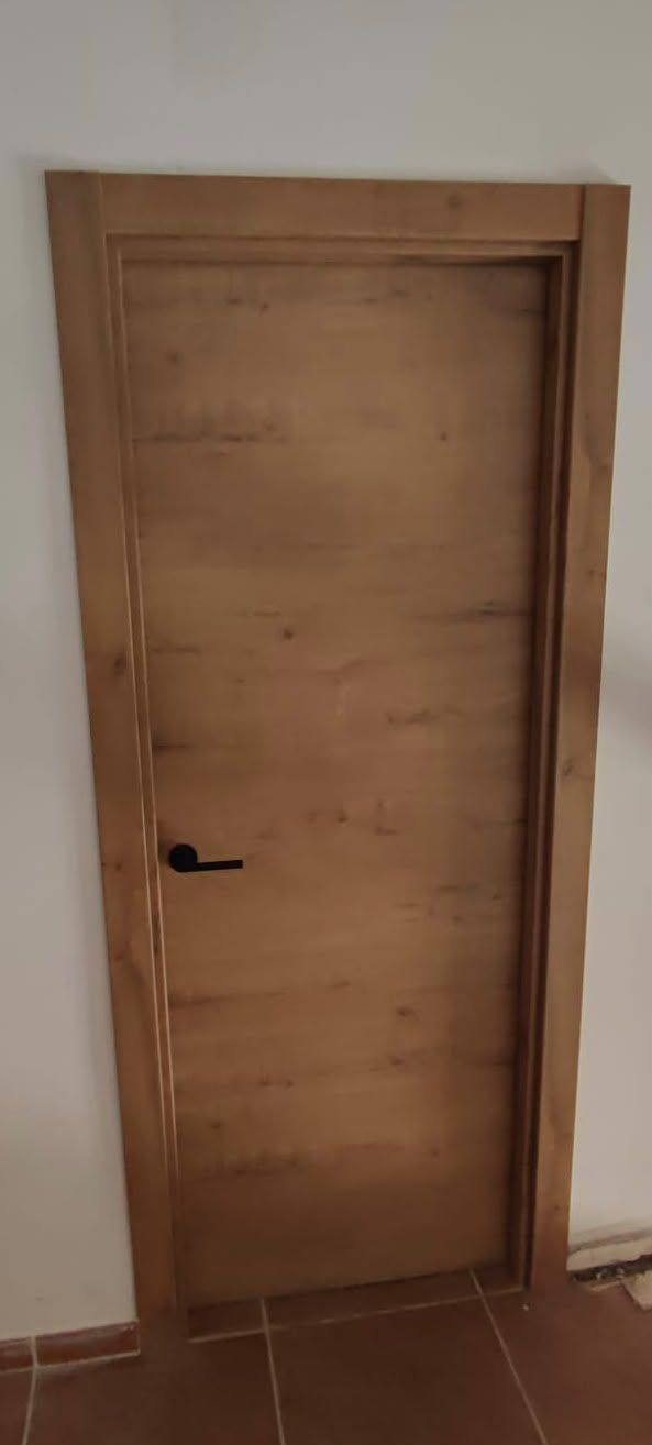 Puerta interior de madera cerrada, con una manija negra y suelo de baldosas marrones