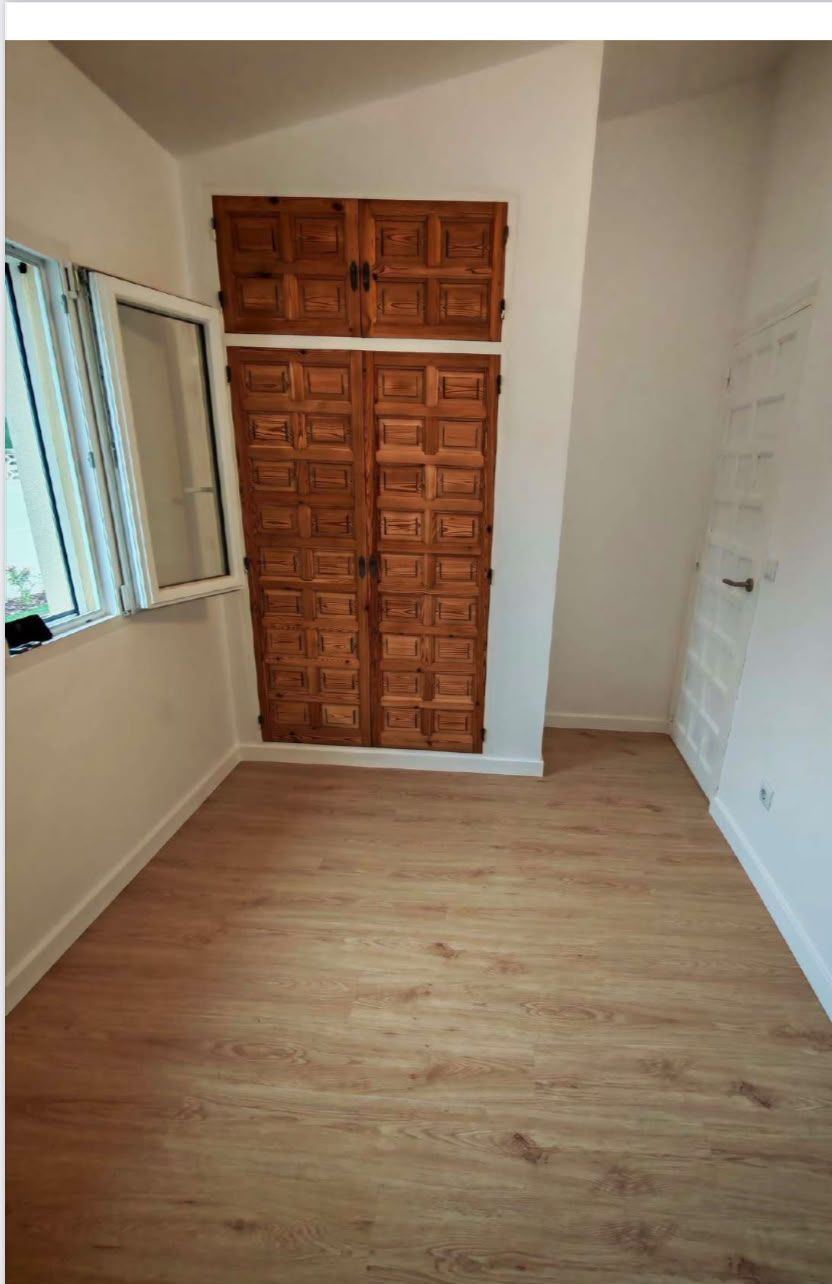Habitación vacía con suelo de aspecto madera, paredes blancas, una ventana y armarios empotrados de madera