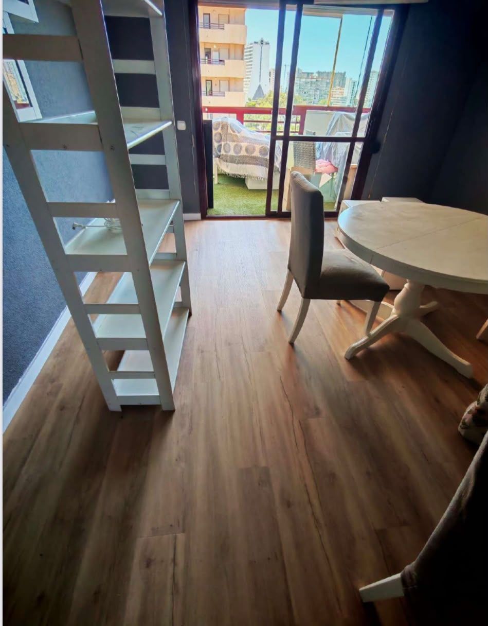 Habitación moderna con escalera de altillo, mesa redonda y sillas, suelo de madera y puertas de balcón
