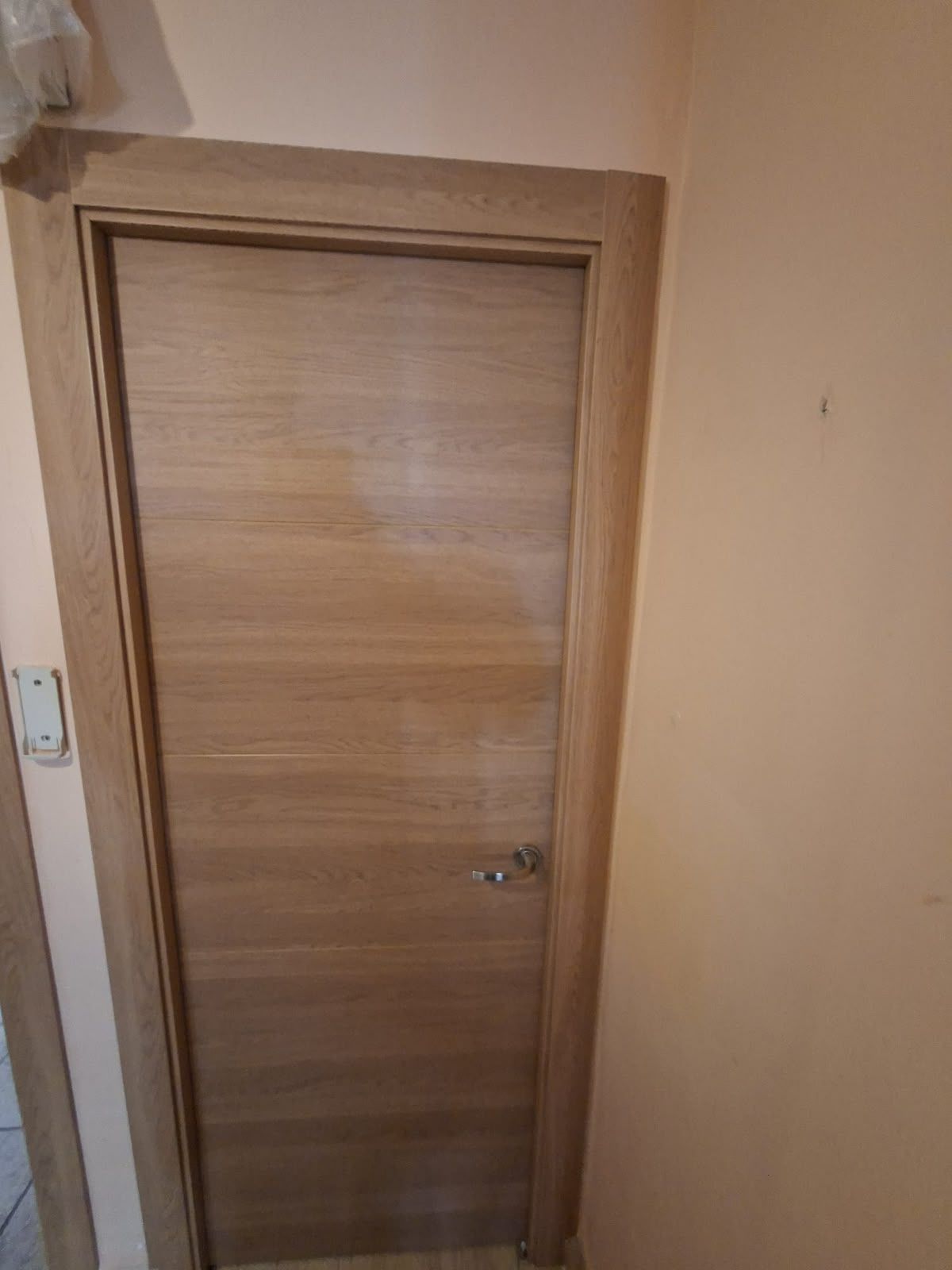 Puerta interior de madera en un pasillo beige con un pequeño interruptor de pared al lado