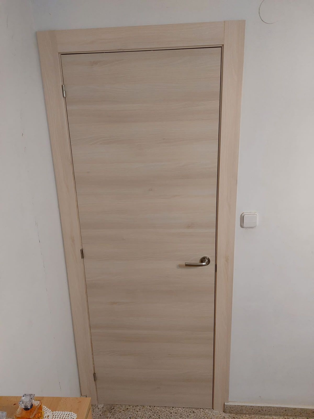 Puerta interior de madera clara con manija plateada en una habitación blanca sencilla