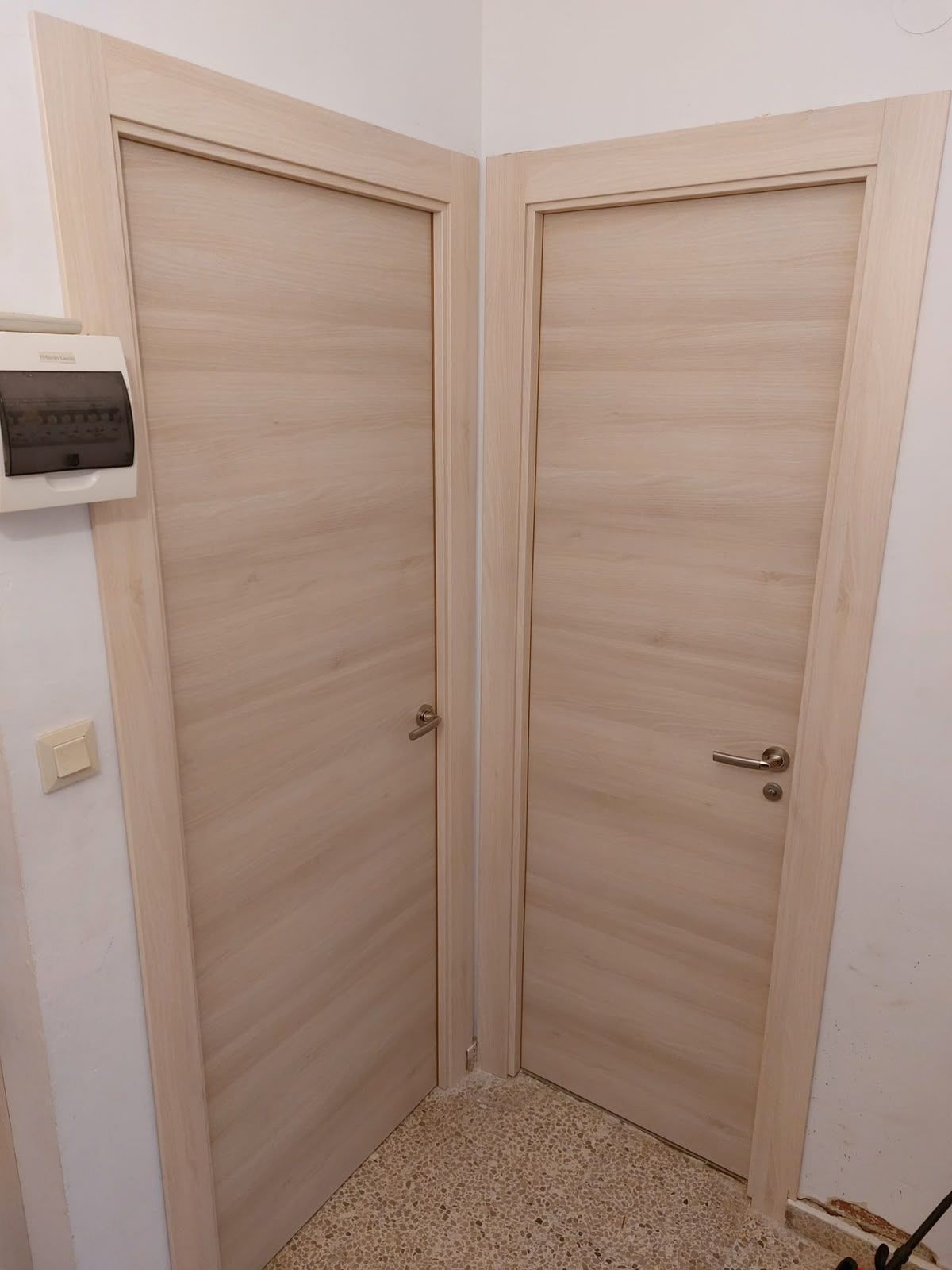 Rincón de un pasillo con dos puertas de madera clara y un termostato en la pared.