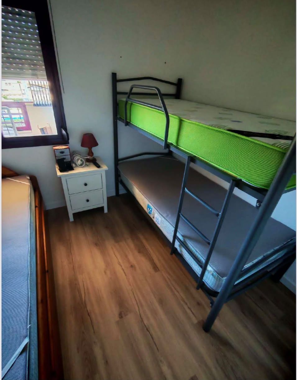 Dormitorio pequeño con una litera negra, un colchón superior verde, una mesita de noche blanca y suelo de madera.