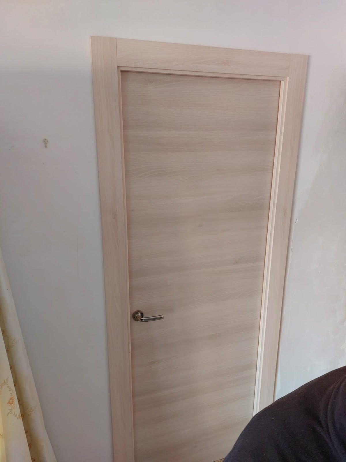 Puerta interior de madera clara con una manilla pequeña, en una pared blanca.