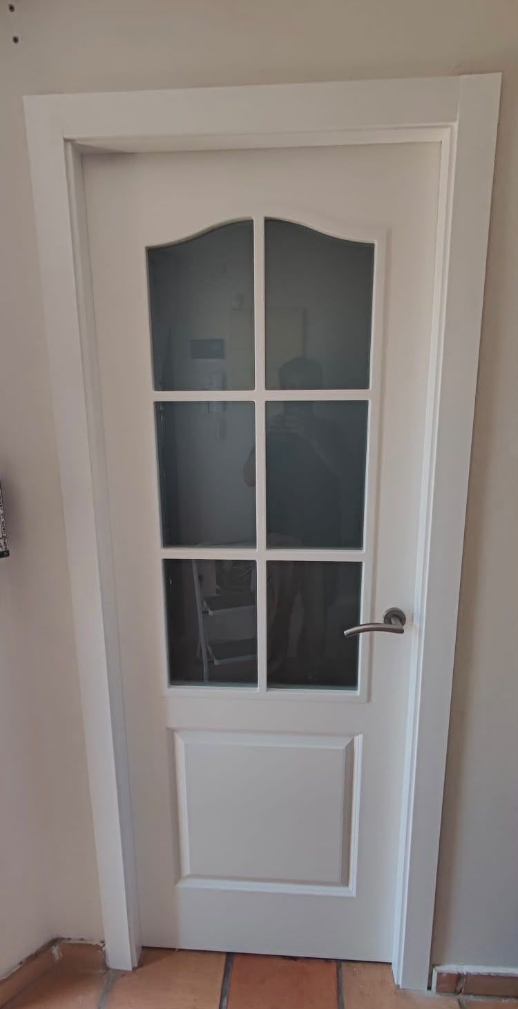 Puerta interior blanca con paneles de vidrio esmerilado y manija plateada en un pasillo