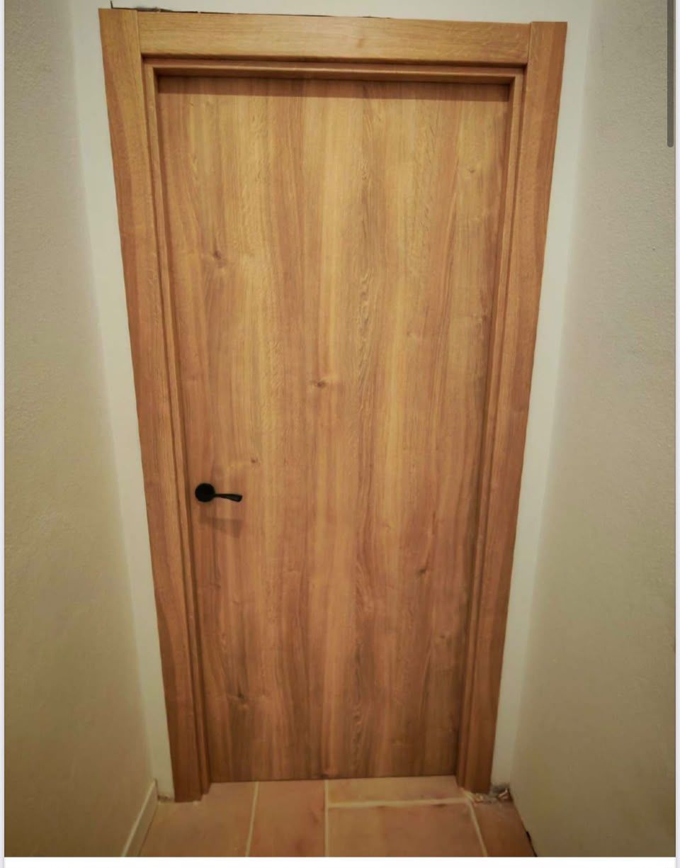 Puerta interior de madera con manija negra en un pasillo beige