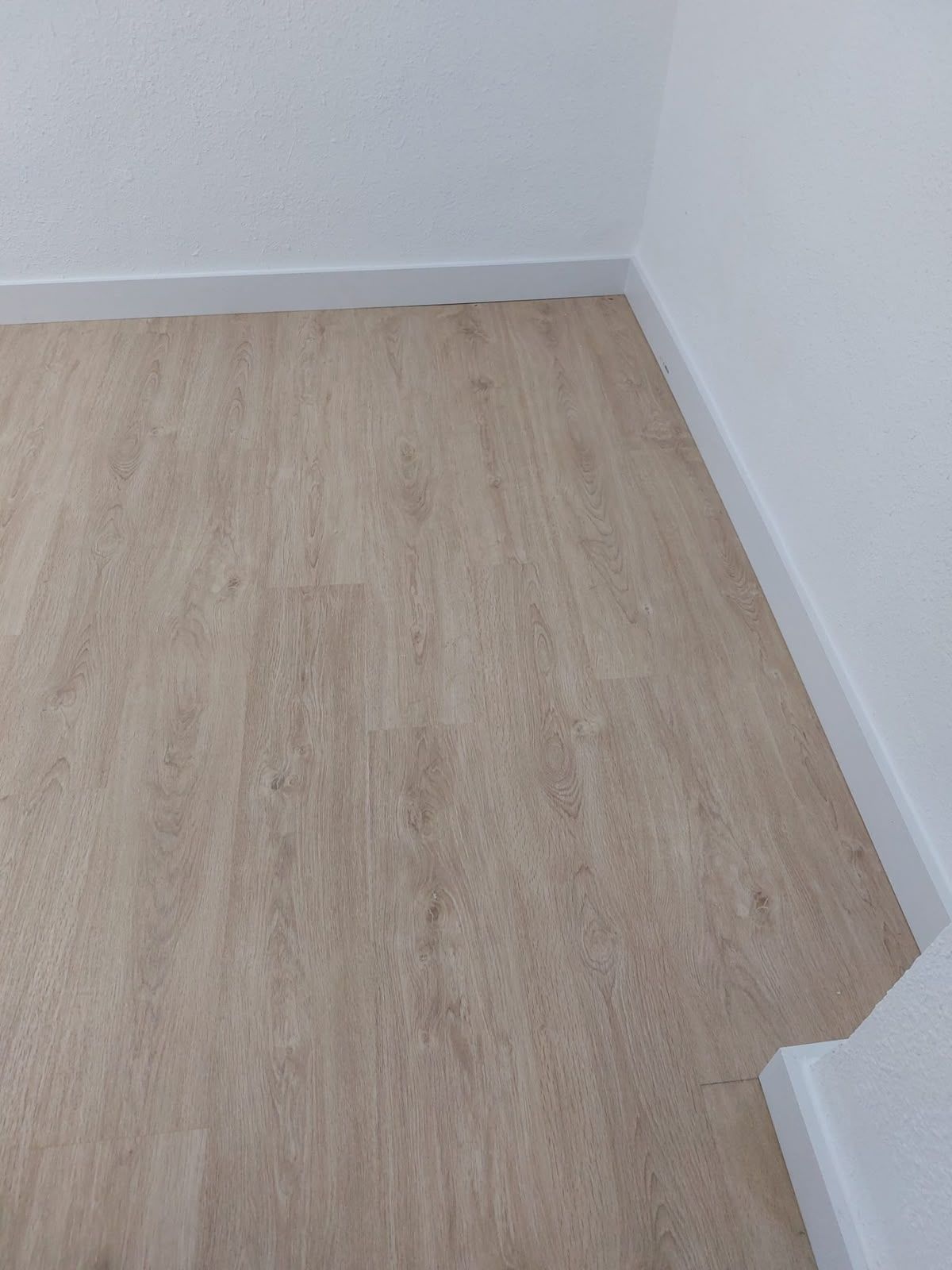 Esquina de una habitación vacía con suelo de madera clara y paredes blancas