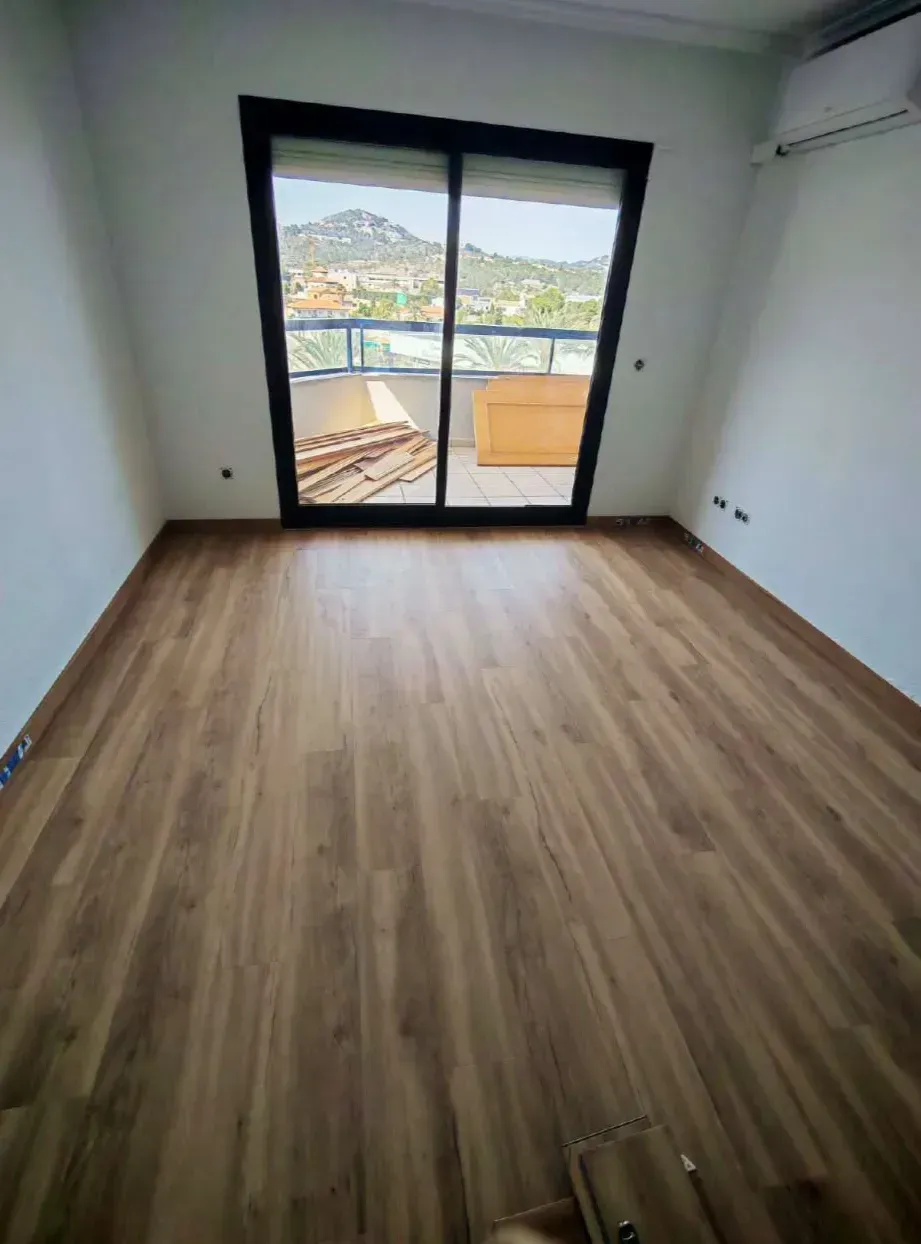Habitación vacía con suelo de madera y puertas correderas de cristal que dan a un balcón con vistas a la montaña