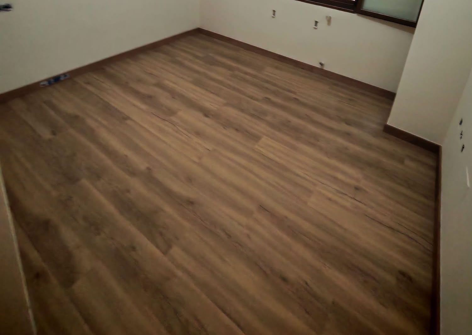 Habitación vacía con suelo laminado de madera y paredes beige, vista desde una esquina.