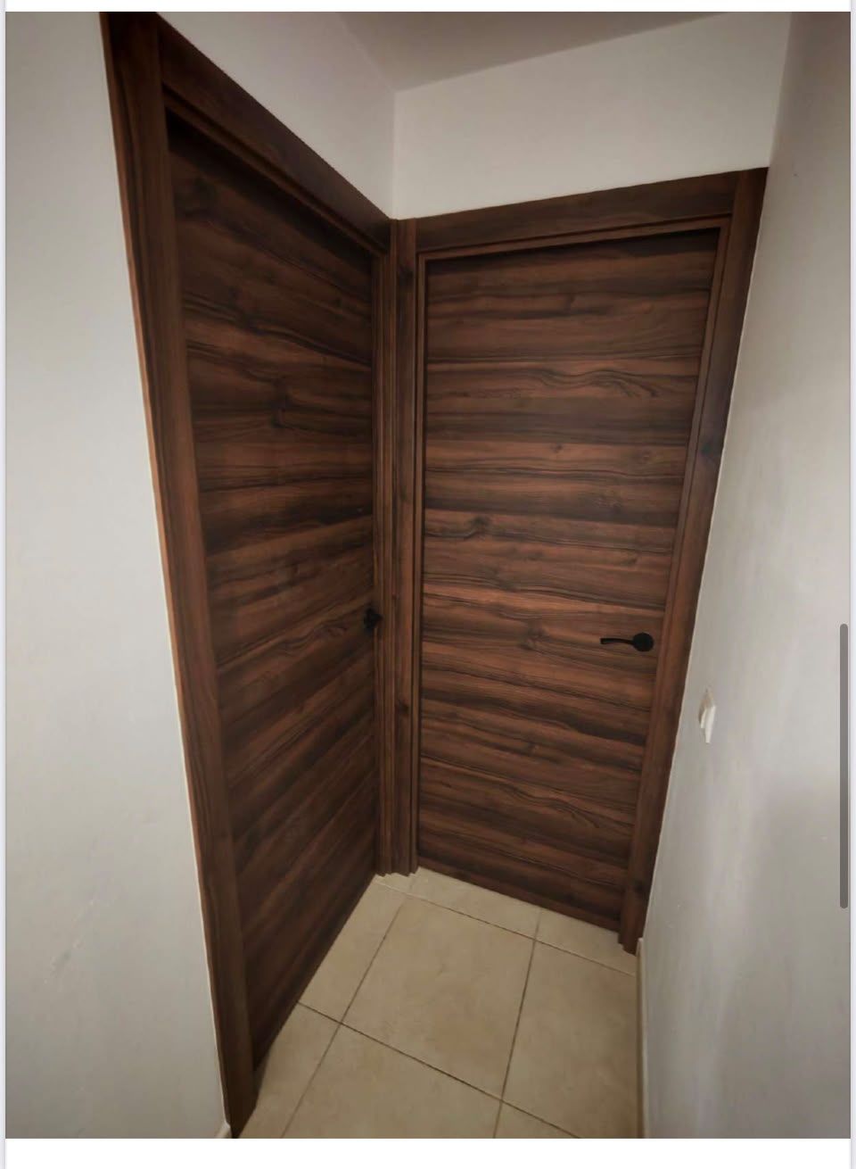 Pasillo estrecho con puertas de madera oscura y suelo de baldosas beige