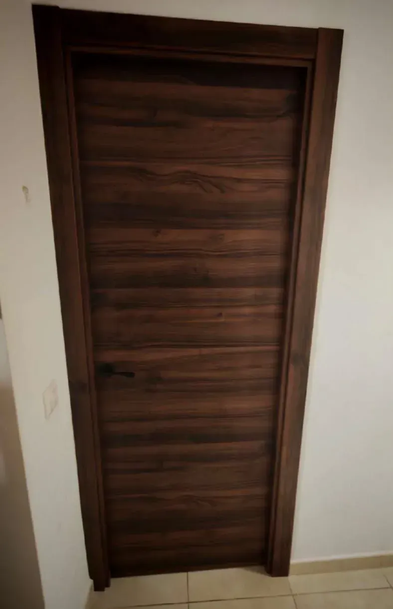 Puerta de madera marrón con paneles horizontales en una pared blanca y suelo de baldosas beige