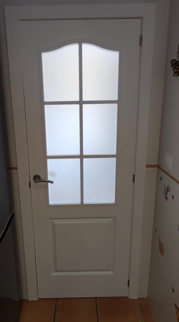 Puerta interior blanca con paneles de vidrio esmerilado y manija plateada en un pasillo