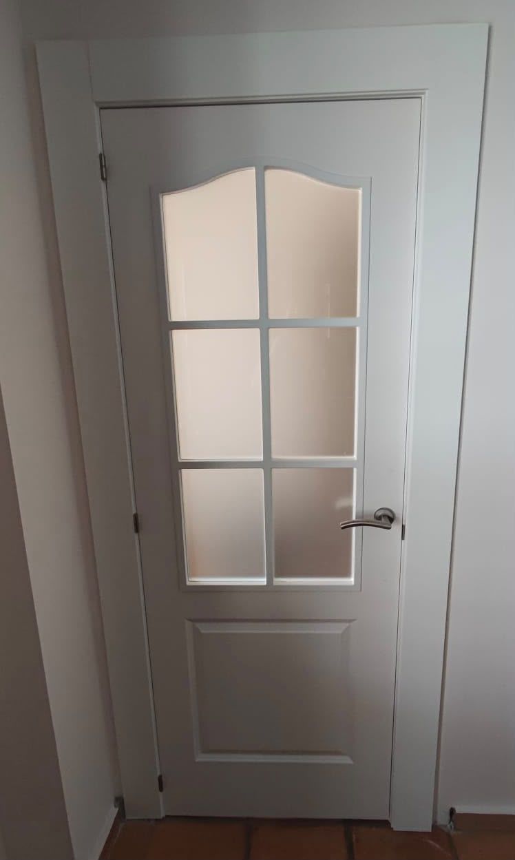 Puerta interior blanca con paneles de vidrio esmerilado y manija plateada en un pasillo