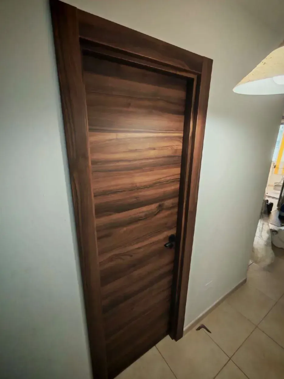 Puerta interior de madera con molduras oscuras en un pasillo embaldosado