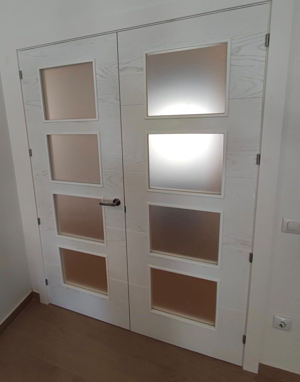 Puertas interiores dobles blancas con paneles de vidrio esmerilado en un pasillo