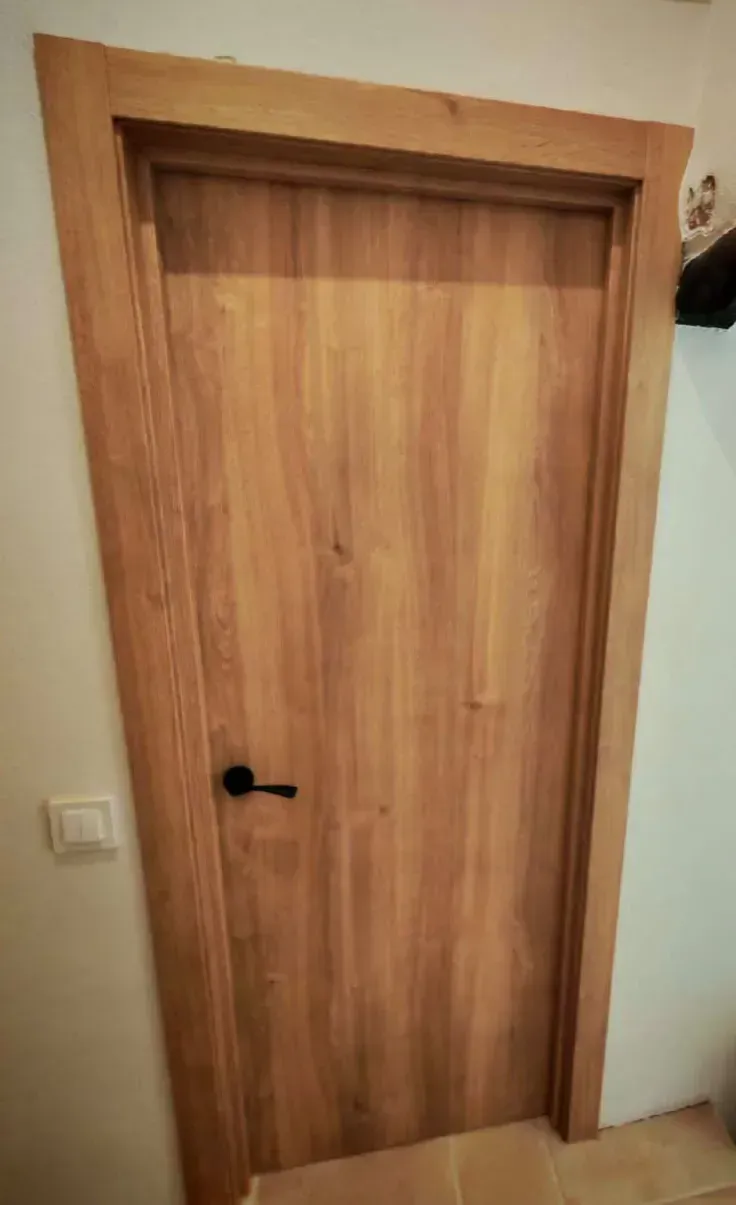 Puerta interior de madera con manilla negra en una pared beige del pasillo