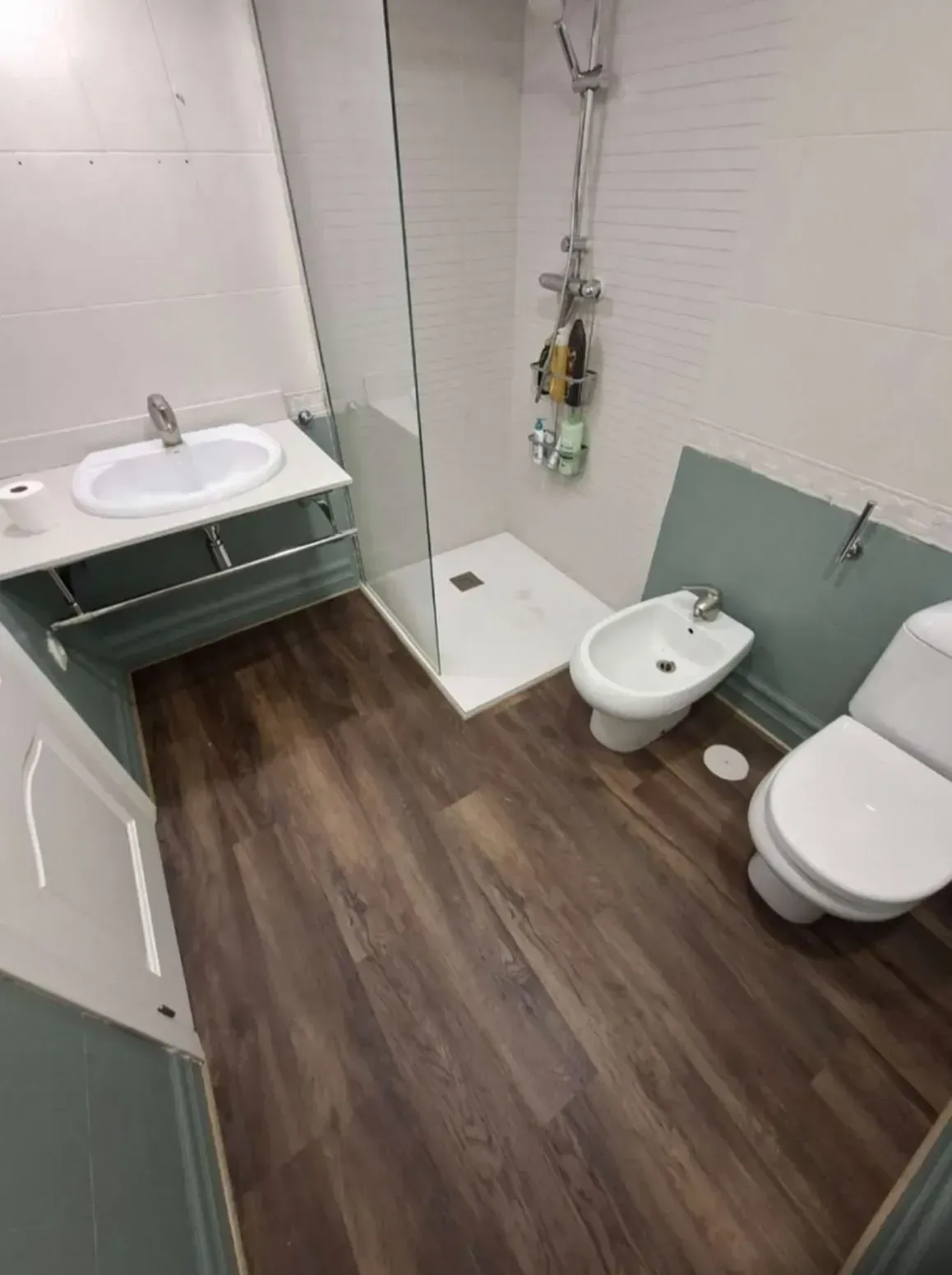 Baño pequeño y accesible con lavabo, inodoro, bidé, ducha y suelo de baldosas con efecto madera.
