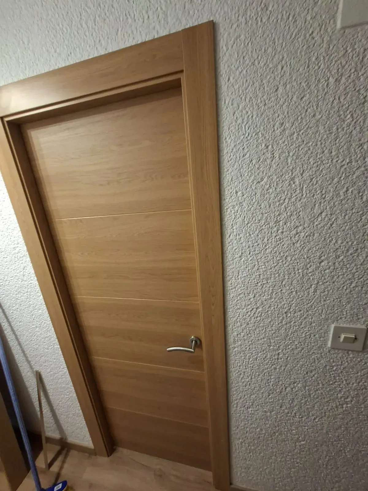 Puerta interior de madera con manija plateada en una pared con textura en el pasillo