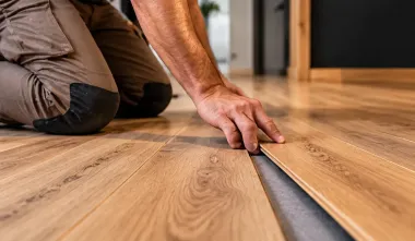 Una persona instalando suelo de madera y alineando una tabla sobre un suelo de madera noble.