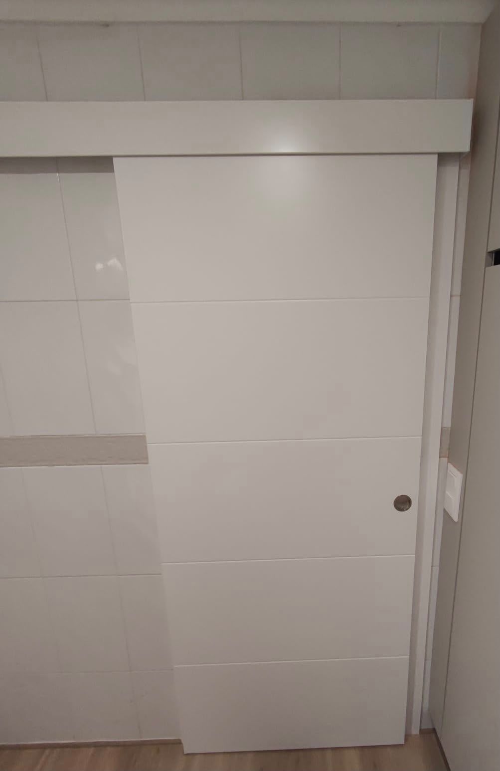 Puerta corrediza blanca de armario en una habitación con azulejos, entreabierta y con un pomo redondo.