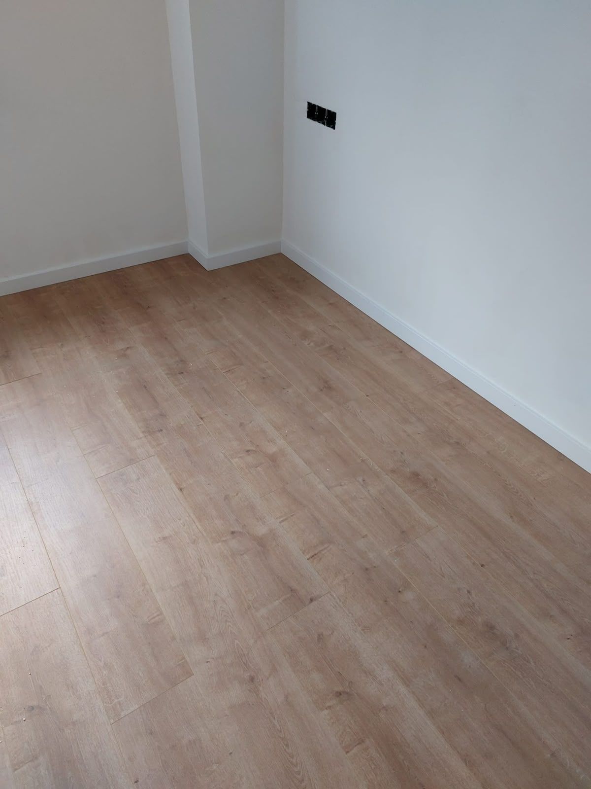 Rincón vacío de una habitación con suelo de madera clara y paredes blancas