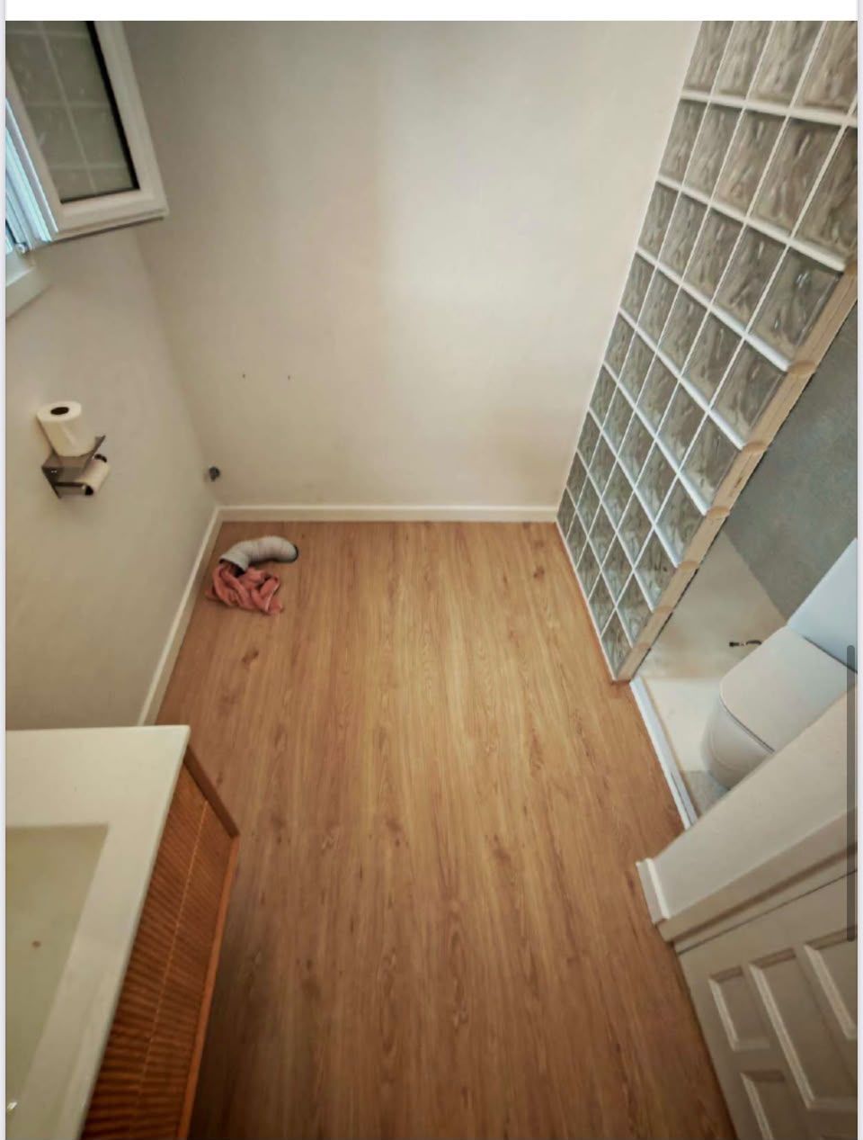 Pequeña habitación vacía con suelo de imitación madera, pared de bloques de vidrio y una toalla en el suelo