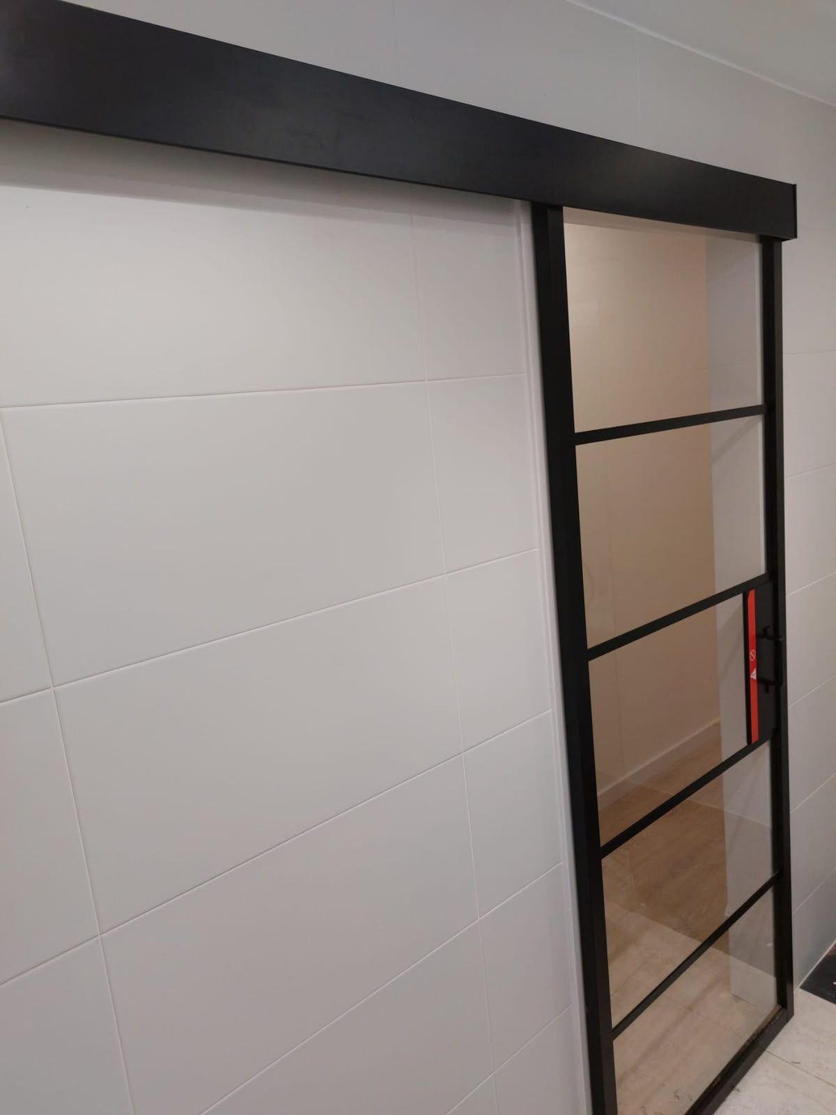 Interior moderno con una puerta corredera de cristal con marco negro junto a una pared blanca con paneles