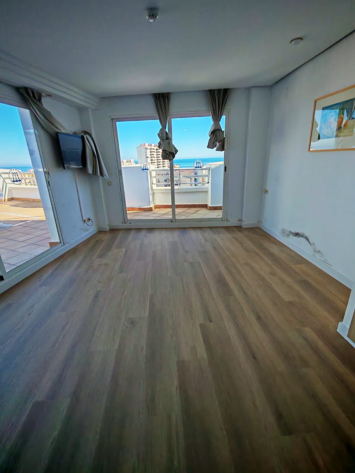 Habitación vacía con suelo de madera, grandes ventanales y vistas a la playa