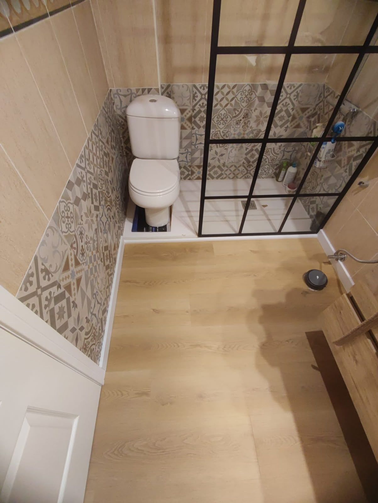 Baño pequeño con inodoro, mampara de ducha y suelo de baldosas efecto madera.