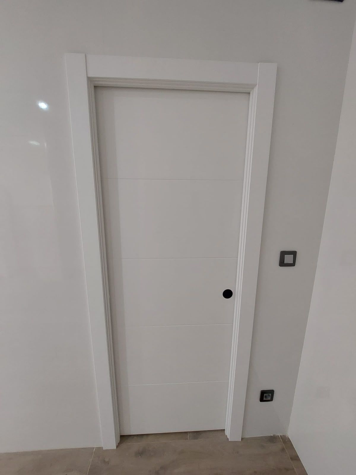 Puerta interior blanca con una manija negra en una pared blanca.