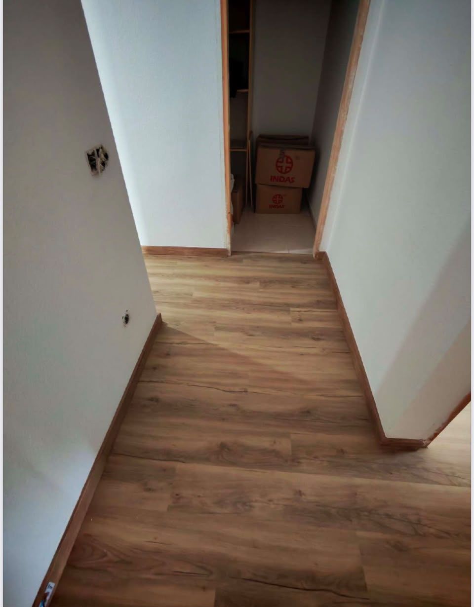 Pasillo estrecho con suelo de imitación madera que conduce a un armario abierto o una zona de almacenamiento con cajas.