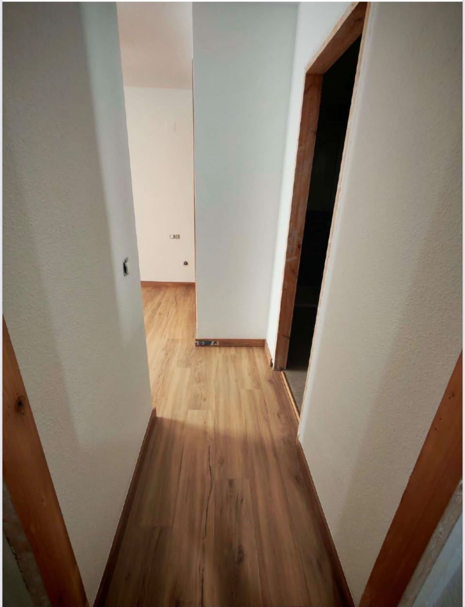 Pasillo estrecho con suelo de madera y paredes blancas, con puertas abiertas a ambos lados.