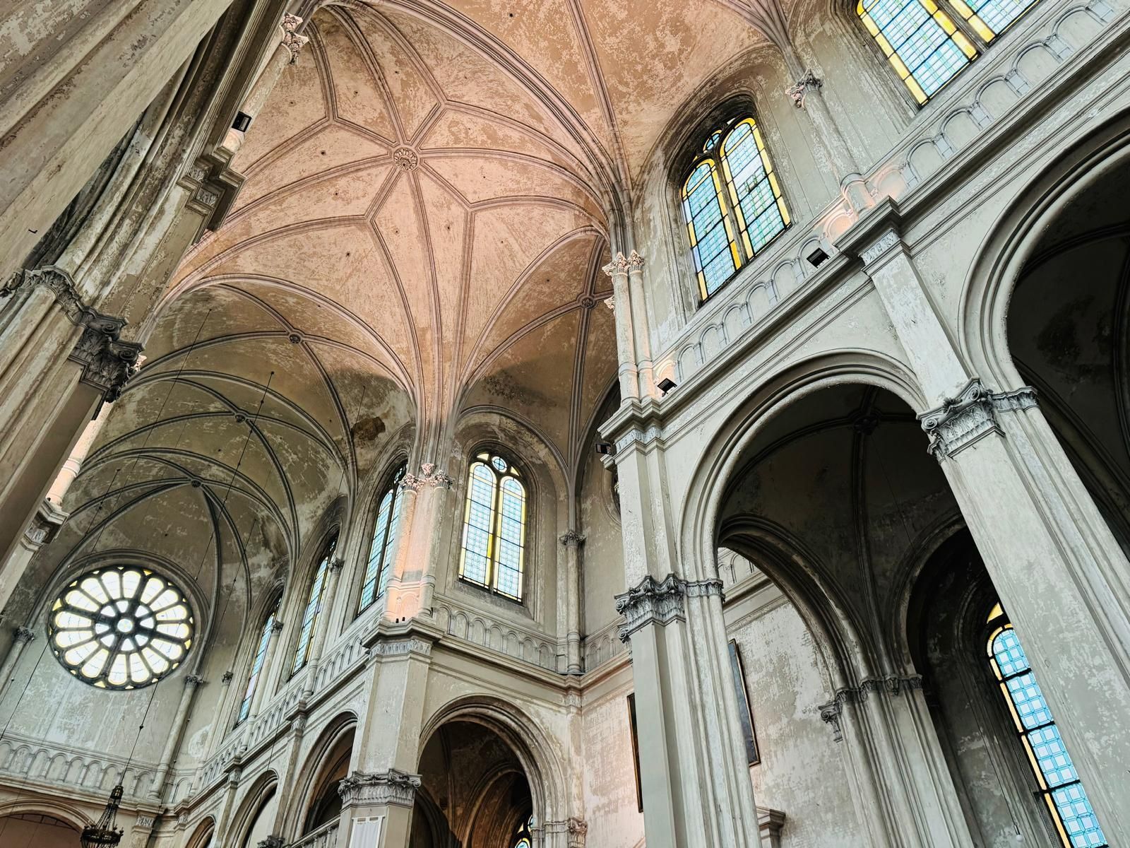 Omhoog kijkend naar het plafond van een kerk met bogen en ramen.