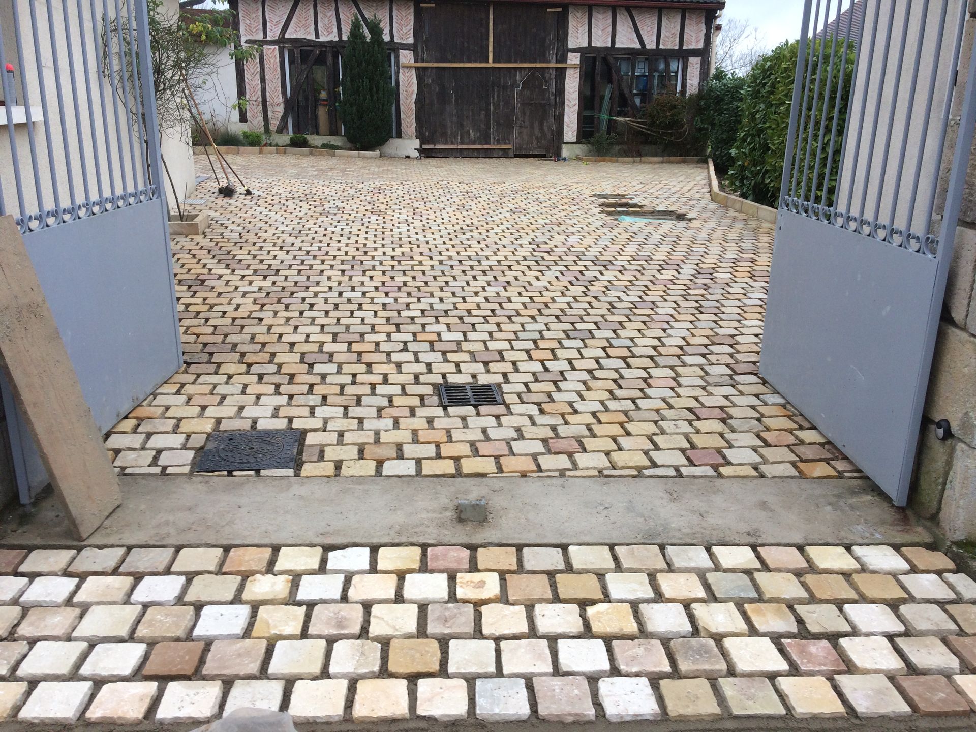 Portail ouvert donnant sur une cour pavée menant à une maison à colombages.